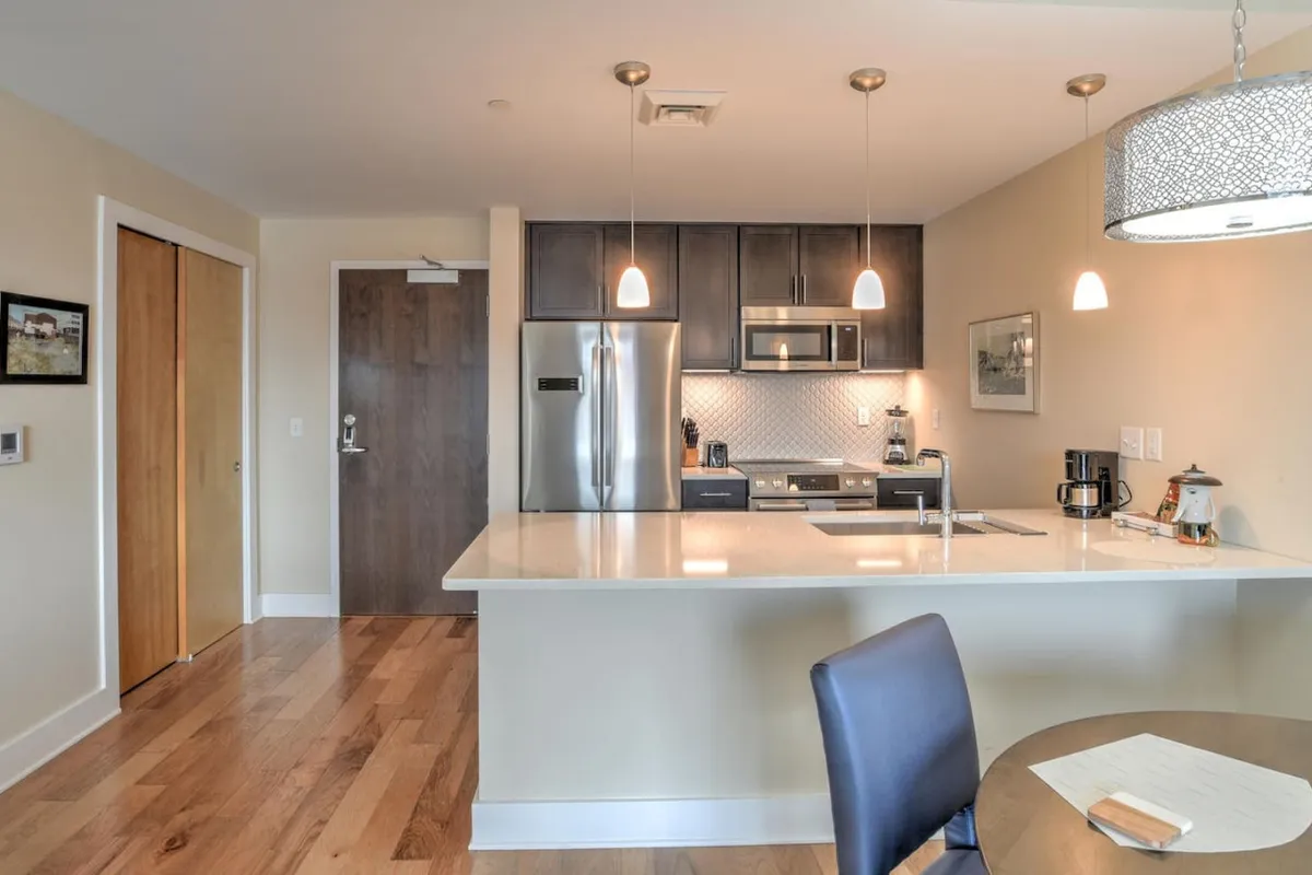 A modern kitchen featuring a spacious island with bar seating, gleaming stainless steel appliances, and stylish pendant lighting. The open layout invites both cooking and socializing, showing plenty of countertop space and contemporary finishes.