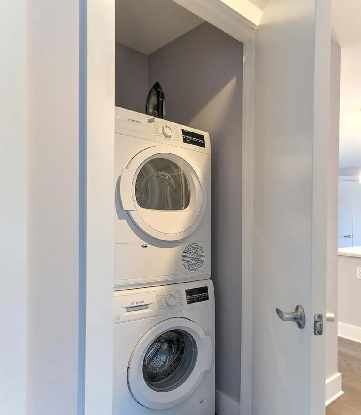 A compact, efficiently organized laundry area featuring a stacked washer and dryer, with an iron thoughtfully placed on top. The setup is clean and practical, emphasizing the ease of handling travel chores on the go.