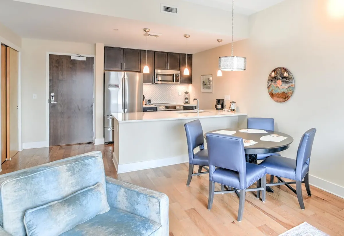 This image captures an open-plan living space with a cozy sofa, a kitchen island, and a dining table. The sofa is prominently positioned, inviting relaxation, while the arrangement suggests a social, welcoming atmosphere. The open flow from the living area to the rest of the space hints at easy movement and communal gatherings.