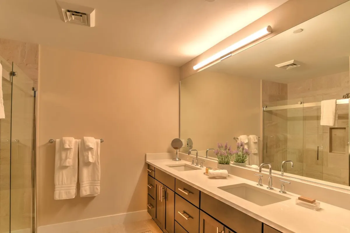 This modern bathroom features a double sink vanity, a framed mirror, a glass shower enclosure, and fresh plants, creating a spa-like atmosphere. The space is bright, organized, and invites moments of relaxation and self-care.
