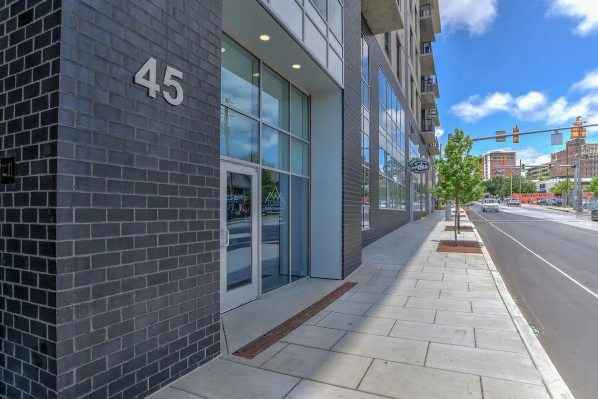 This image captures the building's modern exterior, clearly showing the entrance door and address number along a welcoming sidewalk. The contemporary facade creates a strong first impression for arriving guests.